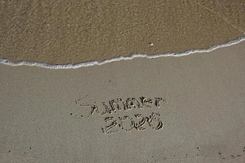 Text written in sand on beach shore with ocean wave approaching Stock Photos