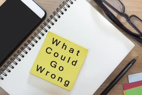 Text on yellow note with notepad on wooden desk - What could go wrong Foto stock