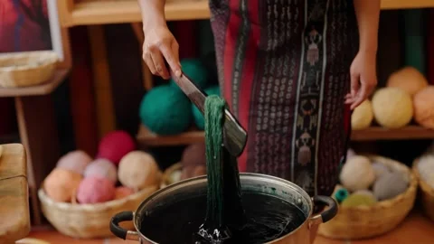 Textile artisan stirs dark dye bath for handmade yarn Stock Footage 329089112