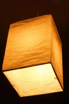 Textile lamp shape of a parallelepiped shines a warm yellow light at night Stock Photos