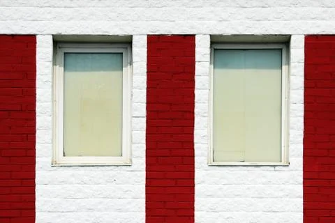 Texture of bright red brick wall with white stripes and windows on a sunny day. Stock Photos