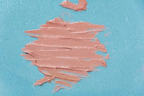 The texture of the foundation is beige under the make-up on a blue background. Stock Photos