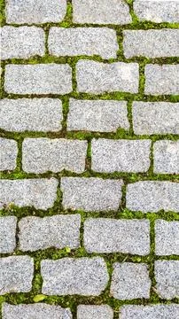Texture of green grass sprouted between bricks of cobblestone path, top view Stock Photos