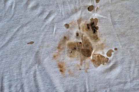 Texture of old dirty torn t-shirt with black-brown spots. Off-white fabric wi Stock Photos