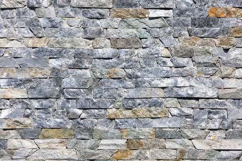 Texture of a stone wall made of granite gray tiles in sunlight. Stock Photos