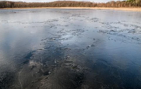 The texture of thin melting ice on a spring lake with the sky reflected on th 写真素材