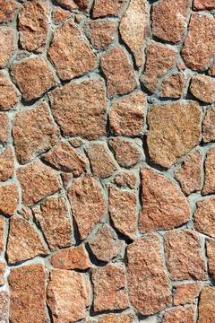 The texture of the wall is lined with red granite stones in the sunlight. Stock Photos