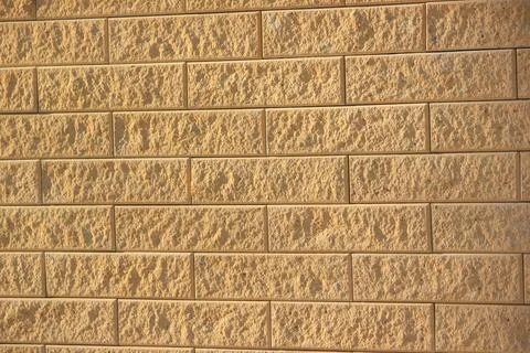 Textured brick wall with a rough surface in warm yellow and orange tones unde Stock Photos