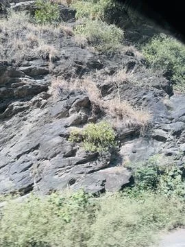 Textured Dark Rock Face with Sparse Hillside Vegetation Stock Photos