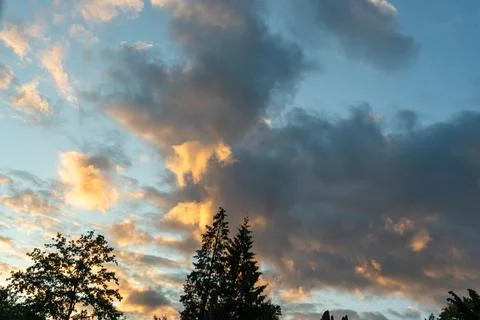Textured evening clouds glowing orange and grey above the dark silhouettes of Stock Photos