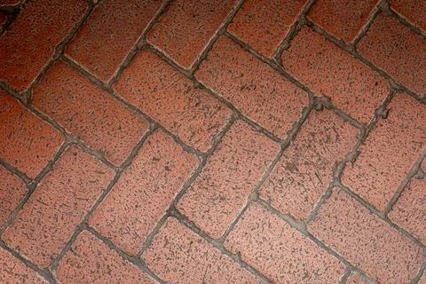 Textured red brick pavement featuring a herringbone pattern in a sunny outdoor Stock Photos