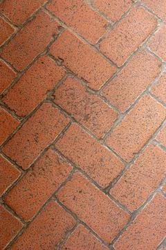 Textured red brick pavement featuring a herringbone pattern in a sunny outdoor Foto stock