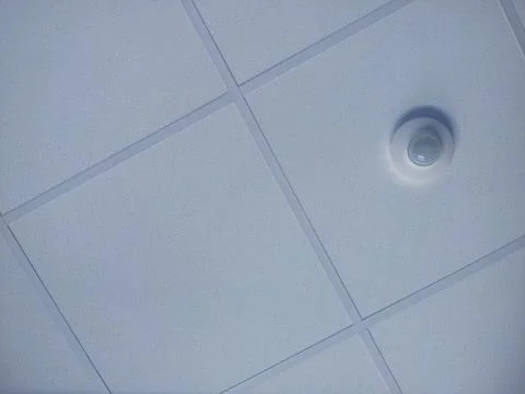 Textured tiles and motion sensor in the t-bar grid of a suspended ceiling Stock Photos