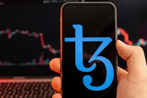 Tezos XTZ cryptocurrency logo on the screen of smartphone in mans hand with Foto stock