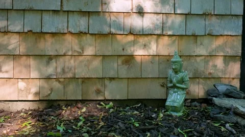 Thai Buddhist Statue Kneeling in Prayer Against Wooden Shingles of a house Stock Footage 337188758