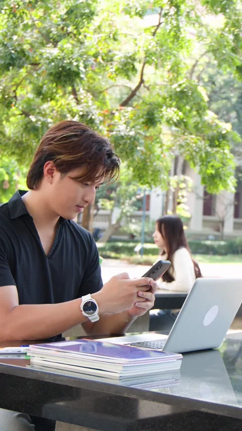 Thai Male Student Using Smartphone at Outdoor University Campus Table Stock Footage 335617162
