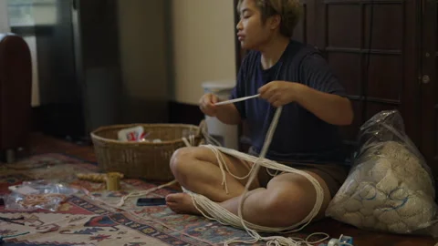 Thai man stringing together pieces of yarn Stock Footage 246597892