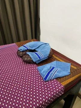 Thai massage room with a patterned mat, blue towels, and a wooden table Stock Photos