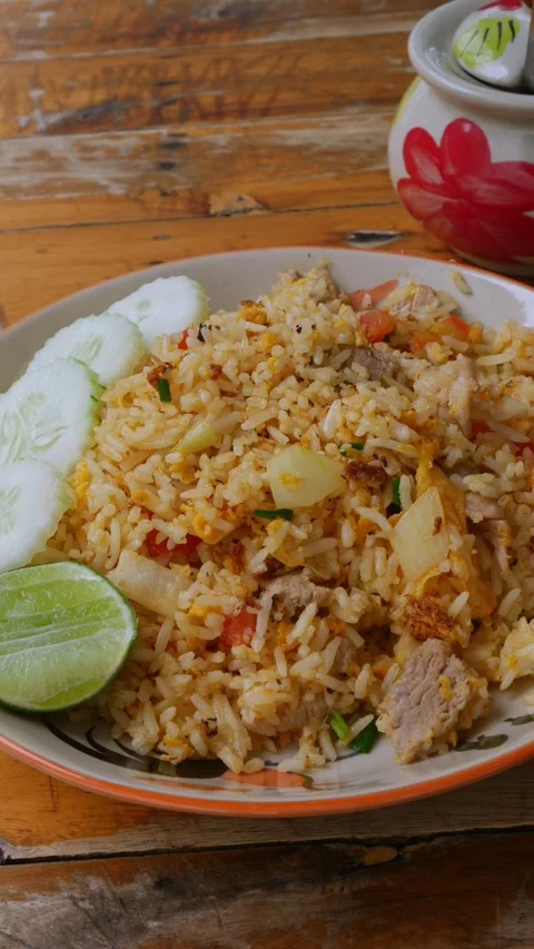 Thai Pork Fried Rice with Cucumber Slices and Lime on Rustic Wooden Table Stock Footage 343234262