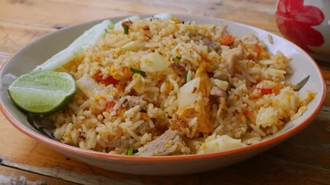 Thai Pork Fried Rice with Cucumber Slices and Lime on Rustic Wooden Table Stock Footage 343609929