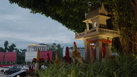 Thai Shrine with Rooster Statues Facing Night Traffic 스톡 동영상 337534400