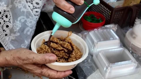 Thai Street Vendor Adding Sauce to Fried Instant Noodles in Takeaway Bowl Stock Footage 335206107
