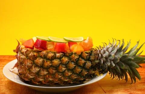 Thai style fruit salad inside a pineapple with a yellow background on a wood tab Stock Photos