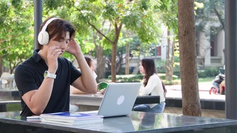 Thai University Student Using Laptop and Headphones on Campus Outdoors 库存影片 329010802
