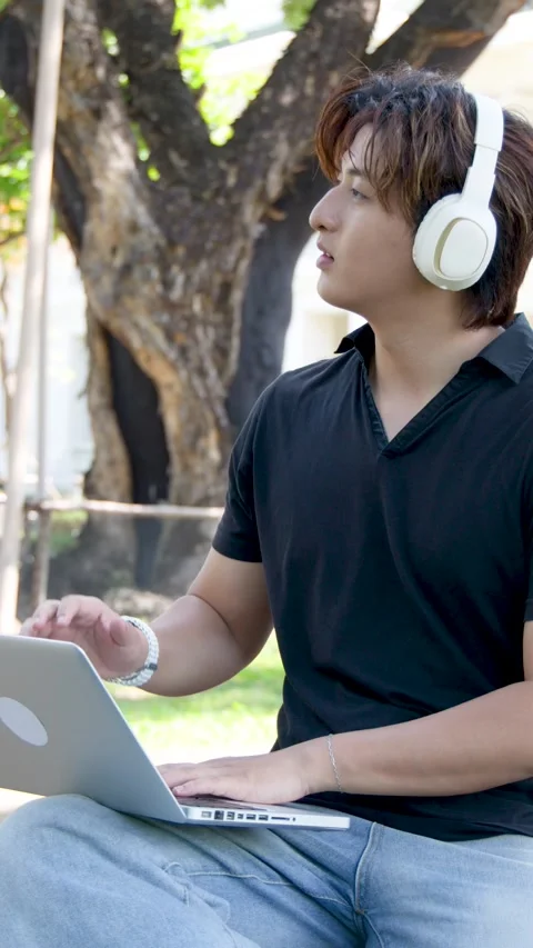 Thai University Student Using Laptop and Headphones Outdoors on Campus Stock Footage 334105200