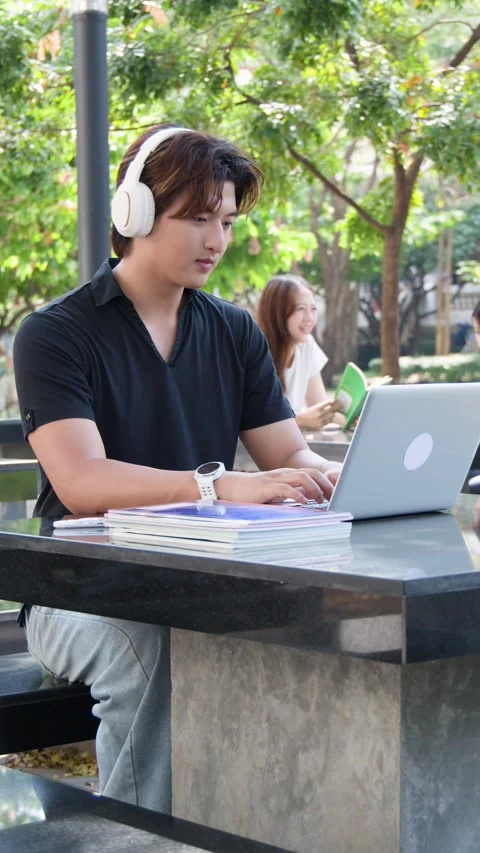 Thai University Student Using Laptop and Headphones on Campus Outdoors Stock Footage 334713254