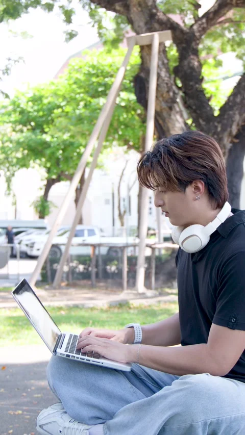 Thai University Student Using Laptop Outdoors on Campus with Headphones Stock Footage 335626573