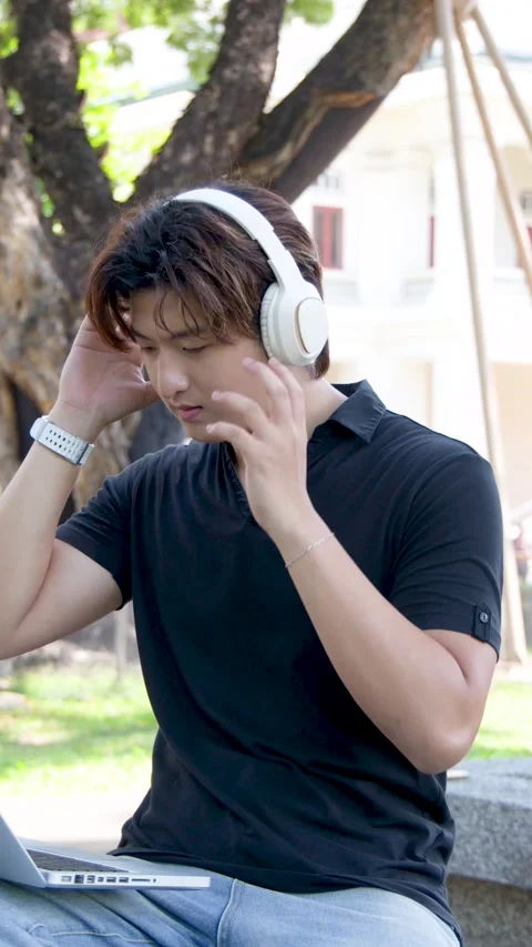 Thai University Student Using Laptop and Headphones on Campus Outdoors Stock Footage 336352237