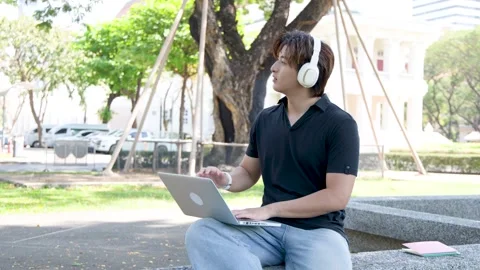 Thai University Student Using Laptop with Headphones on Campus Outdoors Stock Footage 337600465