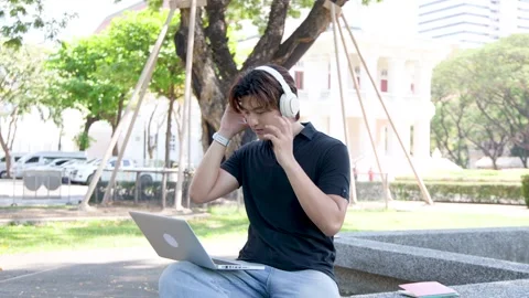 Thai University Student Using Laptop and Headphones on Campus Outdoors Stock Footage 337600518