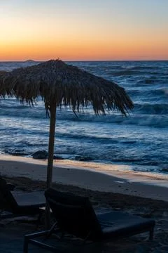 Thatch beach umbrella and sunbed against wavy sea sunset Fotos Stock