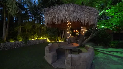 Thatched palapa over a round stone table and bench in a garden Stock Footage 345538170