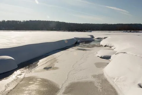 Thawed patch with water on river among snow Stock Photos