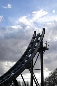 Theme park rollercoaster ride and blue cloudy sky above trees Stock Photos