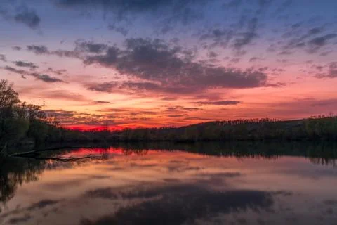 Themed sunset on a pond with a reflection of dark clouds and an orange-red gl Фото