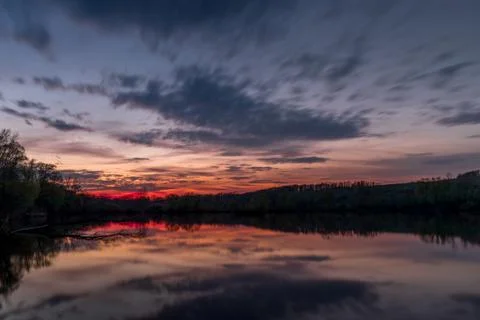 Themed sunset on a pond with a reflection of dark clouds and an orange-red gl Stock-Fotos