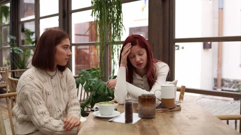 A therapist and her client sit in a calm cafe the client holds her head exhauste Stock Footage 320827335