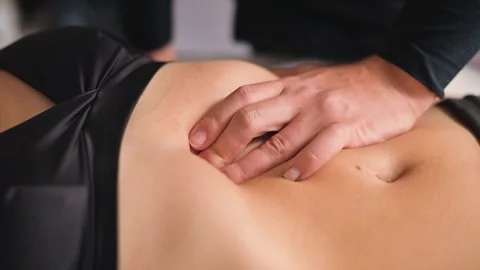 Therapist performs a manual technique on a patient's lower back to promote Vídeos de archivo 344379906
