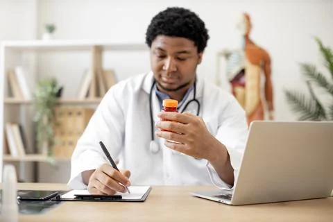 Therapist taking notes about pills using computer in clinic 스톡 사진