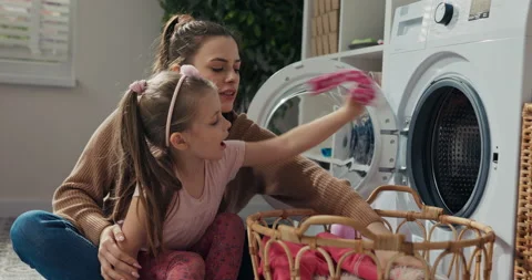 There are dirty clothes in laundry basket. Smiling girl and mother throw clothes 库存影片 218314573