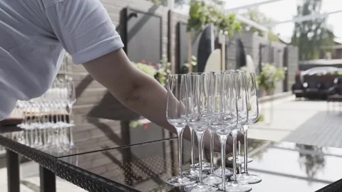 There are empty champagne glasses on an open-air wooden table. The waiter puts Stock-Footage 306144800