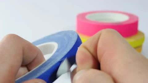 There are many colored teips on the table. A man's hand tears off a piece of Stock Footage 188318933