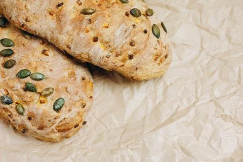 There are two loaves of bread with some seeds on the paper. Stock Photos