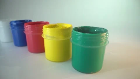 There are white, blue, red, green and yellow jar of paint on the table. Artist Stock Footage 141368190