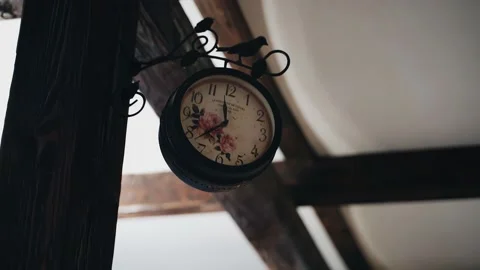 There is a clock hanging on a wooden column in the building under the ceiling Vídeos de archivo 231561484