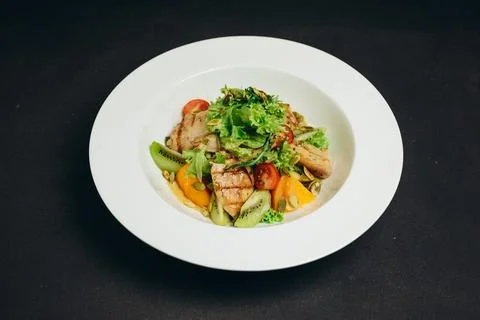 There is a dish that includes some kiwi, tomatoes, green and meat. Stock Photos